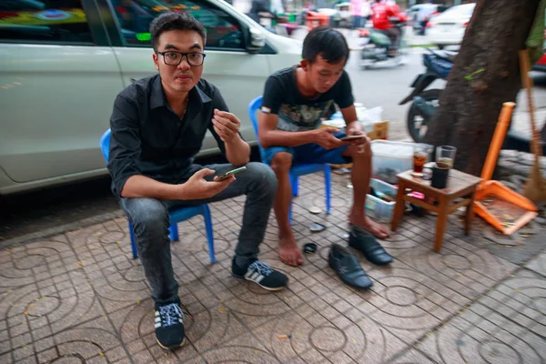 Ho Chi Minh şehri, Vietnam - Aralık 2018: Yoldaki küçük mavi sandalyelerde oturan ve cep telefonlarını izleyen iki Vietnamlı adam.
