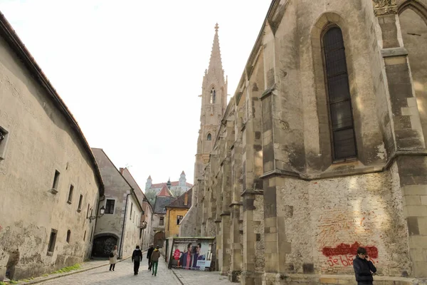 Bratislava, Slovakya - Nisan 2011: Farska Caddesi 'ndeki insanlar, binalar ve Kutsal Haç Yükselişi Kilisesi.