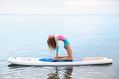 Woman doing yoga on sup board with paddle clipart