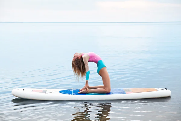 Frau macht Yoga auf Surfbrett mit Paddel — Stockfoto