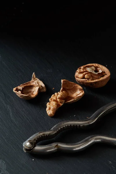 Walnuts and kernels on a black backdrop with nutcracker — Stock Photo, Image