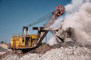 Büyük bir taş ocağı kova ekskavatör sıcak bir açık havada cüruf dökümü çalışır. Ağır endüstriyel metalurjik sisli manzara