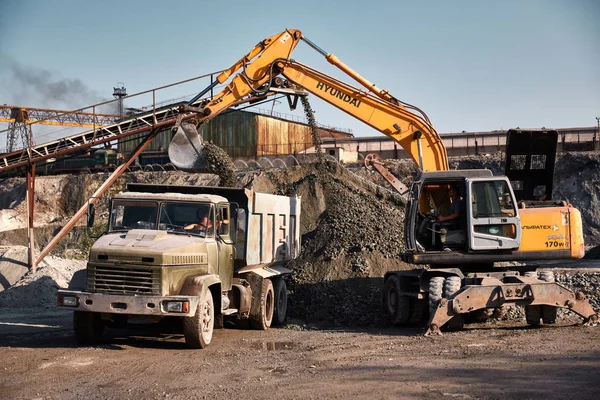 Kova ekskavatör sıcak bir açık havada cüruf dökümü çalışır. Arka planda demiryolu yolu ve tren ile ağır endüstriyel metalurjik sisli manzara