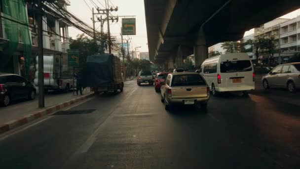 Bangkok Thajsko - 06. ledna 2020: Auta stojí a pomalu řídí v dopravní zácpě pod dálnicí. Brzy ráno, záře slunce na sloupech mostu. — Stock video