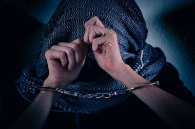 Genç bir kadın şiddete maruz kalıyor, ellerini kelepçeleyerek yüzünü kapatıyor. Elleri damarlar ve yaralarla dolu, kafasında bir bez parçası