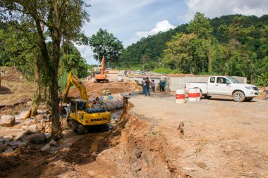 Chiangrai / Tayland - 20 Ağustos 20018, sel sonrası yol rehabilitasyonu, nehirde çalışan sarı kazıcı, Chiangrai - Chiangmai yolu 118