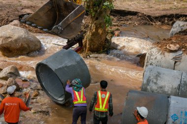 Chiangrai / Tayland - 20 Ağustos 20018, sel sonrası yol rehabilitasyonu. İşçiler kazıcının kovasına beton boru döker ve Chiangrai - Chiangmai yolu 118 'e yerleştirirler.