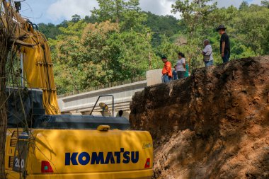 Chiangrai / Tayland - 20 Ağustos 20018, sel sonrası yol rehabilitasyonu. Köylüler uçurumun kenarında duruyorlar ve kazıcının çalışmalarına bakıyorlar, Chiangrai - Chiangmai Yolu 118