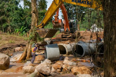 Chiangrai / Tayland - 20 Ağustos 20018, sel sonrası yol rehabilitasyonu. İşçiler kazıcının kovasına beton boru döker ve Chiangrai - Chiangmai yolu 118 'e yerleştirirler.
