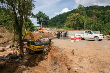 Chiangrai / Tayland - 20 Ağustos 20018, sel sonrası yol rehabilitasyonu, nehirde çalışan sarı kazıcı, Chiangrai - Chiangmai yolu 118