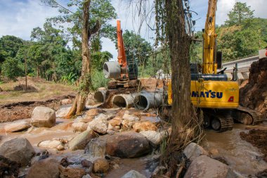 Chiangrai / Tayland - 20 Ağustos 20018, sel sonrası yol rehabilitasyonu. İki kazıcı ve üç işçi, Chiangrai - Chiangmai yolu 118 'de suyu boşaltmak için beton borular döşüyorlar.