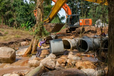 Chiangrai / Tayland - 20 Ağustos 20018, sel sonrası yol rehabilitasyonu. İşçiler kazıcının kovasına beton boru döker ve Chiangrai - Chiangmai yolu 118 'e yerleştirirler.