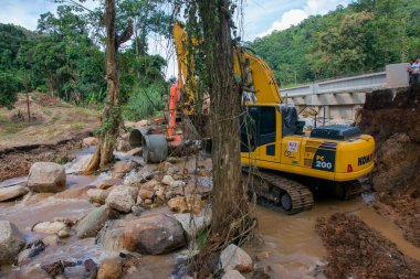 Chiangrai / Tayland - 20 Ağustos 20018, sel sonrası yol rehabilitasyonu, nehirde çalışan sarı kazıcı, Chiangrai - Chiangmai yolu 118