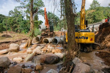 Chiangrai / Tayland - 20 Ağustos 20018, sel sonrası yol rehabilitasyonu. İki kazıcı ve üç işçi, Chiangrai - Chiangmai yolu 118 'de suyu boşaltmak için beton borular döşüyorlar.