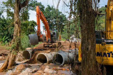 Chiangrai / Tayland - 20 Ağustos 20018, sel sonrası yol rehabilitasyonu. İki kazıcı ve üç işçi, Chiangrai - Chiangmai yolu 118 'de suyu boşaltmak için beton borular döşüyorlar.