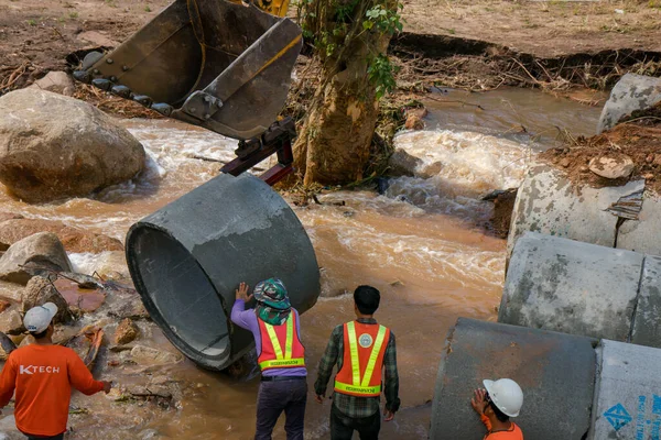 Chiangrai /Thailand - August 20, 20018, road rehabilitation after flooding. Workers chop the concrete pipe to the bucket of the excavator and install it in the river, Chiangrai - Chiangmai road 118