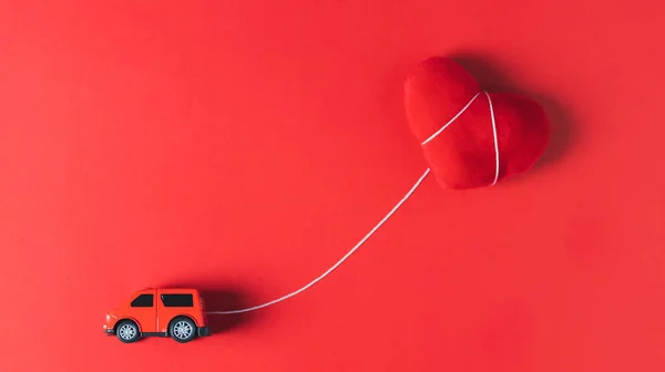 A red car model towing a red heart pillow