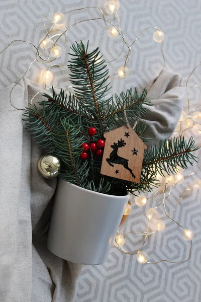 Noel ve Yeni Yıl kompozisyonu. Gri arka planda, köknar dalları ve Noel ışıkları olan hafif bir bardak..