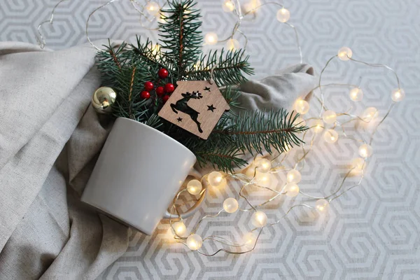 Noel ve Yeni Yıl kompozisyonu. Gri arka planda, köknar dalları ve Noel ışıkları olan hafif bir bardak. Kış kartı. Yumuşak odak