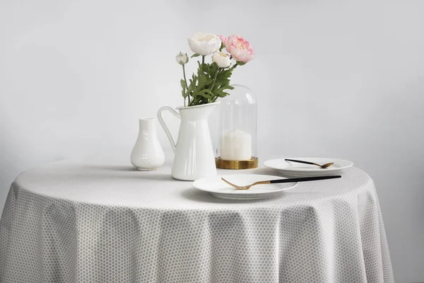 Çiçekli yuvarlak masa, hafif masa örtüsü ve hafif arka planda tabaklar..