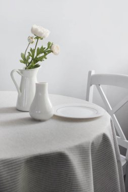 Tabakları ve çiçekleri olan parlak renkli bir masa. Yuvarlak masa, beyaz arkaplanda hafif bir masa örtüsü var..