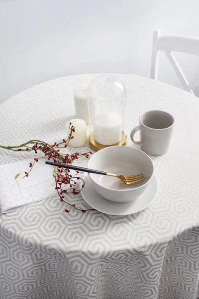 Masada beyaz bir masa örtüsü ve kırmızı böğürtlen dalı olan tabaklar yuvarlak masa, daire içi parlak renklerde servis ediliyor.