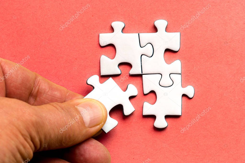 White pieces of a jig saw puzzle on a red background, a hand placing the fitting piece