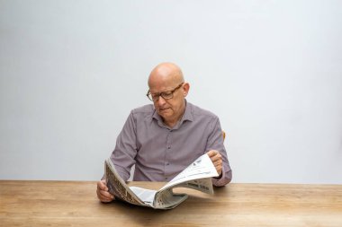 Beyaz erkek, masa başında oturmuş bir fincan kahve içerken gazete okuyor..