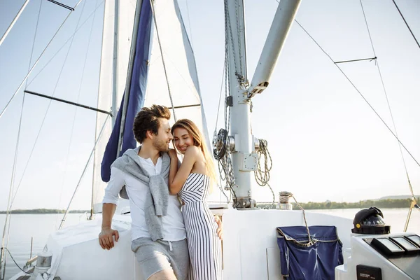 Beautiful young couple on a sailing yacht at sunset. Light clothes, shorts and a trouser suit. Hug and laugh