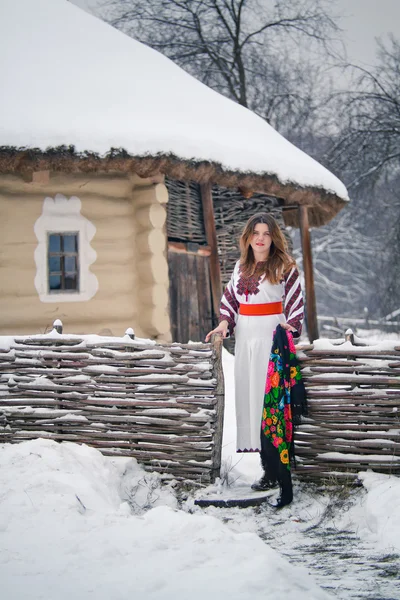 Fille ukrainienne en costume national sur fond d'hiver avec des bâtiments ethniques — Photo