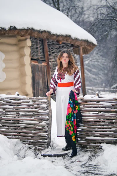Ukrainisches Mädchen in Tracht auf winterlichem Hintergrund mit ethnischen Gebäuden — Stockfoto