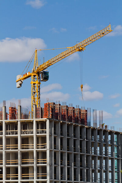 Yellow construction tower crane and house under construction