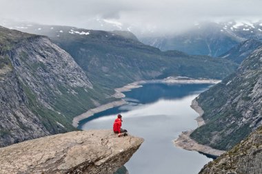 Kamera Trolltunga kaya (Troll dil rock) üzerinde oturan ve Norveç dağ manzarası arayan adam