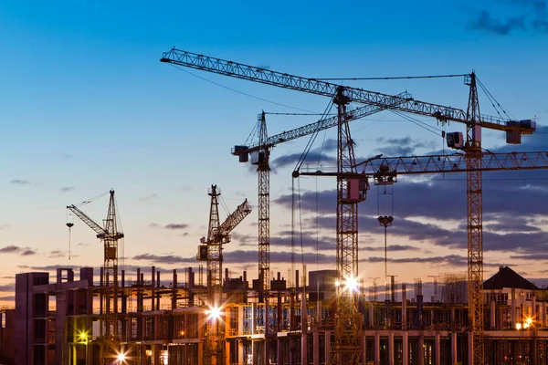 Silhuetas de guindastes de torre contra o céu da tarde. Casa em construção. Linha do horizonte industrial — Fotografia de Stock