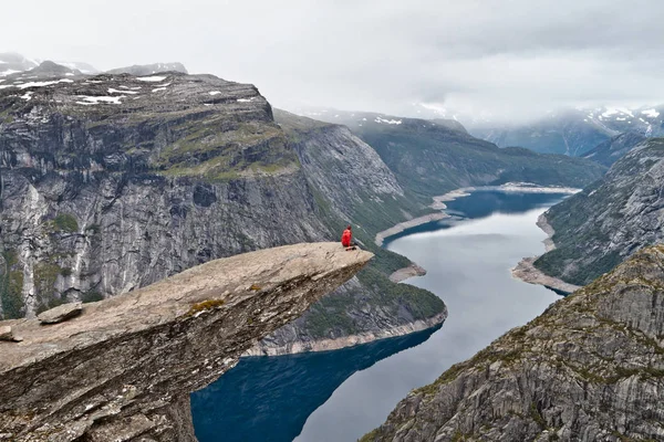 Mann mit Kamera sitzt auf Trolltunga-Felsen (Trollzungenfelsen) und blickt auf norwegische Berglandschaft — Stockfoto