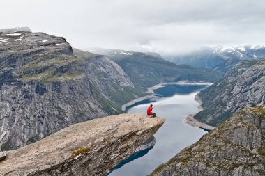 Kamera Trolltunga kaya (Troll dil rock) üzerinde oturan ve Norveç dağ manzarası arayan adam