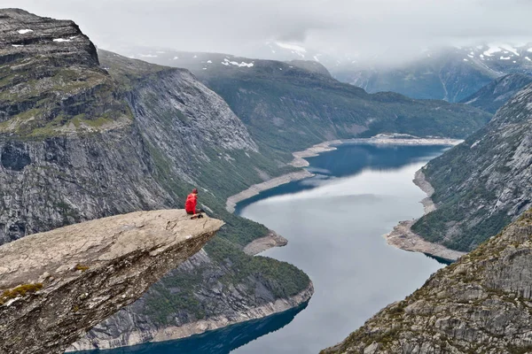 Mann mit Kamera sitzt auf Trolltunga-Felsen (Trollzungenfelsen) und blickt auf norwegische Berglandschaft — Stockfoto