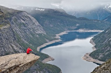 Adam ile Trolltunga rock (Troll dil rock) üzerinde oturan fotoğraf makinesi ve fotoğraf Norveç dağ manzarası ile yapar