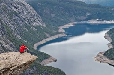 Adam ile Trolltunga rock (Troll dil rock) üzerinde oturan fotoğraf makinesi ve fotoğraf Norveç dağ manzarası ile yapar