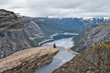 Trolltunga kaya (Troll dil rock) üzerinde oturan ve Norveç dağ manzarası arayan kız