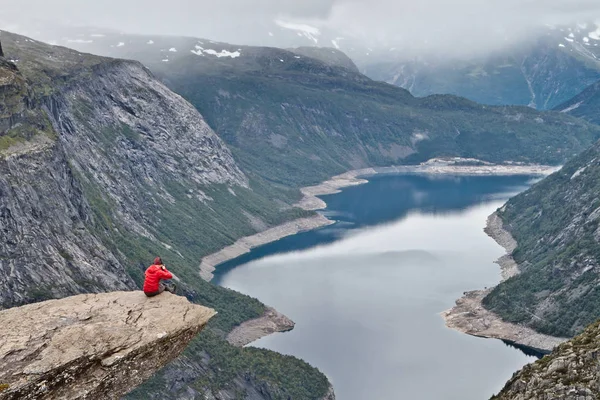 Homem com câmera sentada na rocha Trolltunga (Rocha da Língua do Troll) e faz a foto com a paisagem montesa norueguesa — Fotografia de Stock