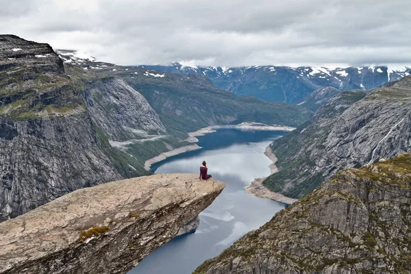 Κορίτσι που κάθεται σε βράχο χώρου (Trolltunga) (Troll του γλώσσα ροκ) και κοιτάζοντας Νορβηγικά ορεινό τοπίο — Φωτογραφία Αρχείου