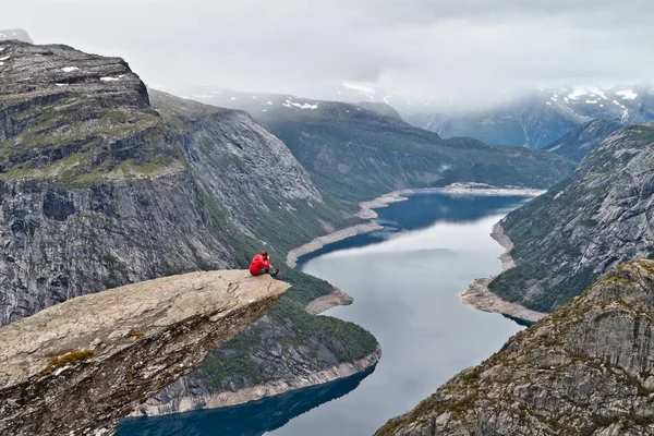 Adam ile Trolltunga rock (Troll dil rock) üzerinde oturan fotoğraf makinesi ve fotoğraf Norveç dağ manzarası ile yapar