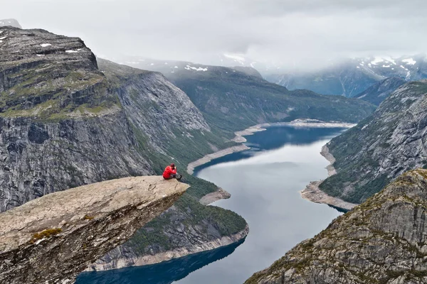 Άνθρωπος με μηχανή κάθεται σε βράχο χώρου (Trolltunga) (Troll του γλώσσα rock) και να κάνει τη φωτογραφία με το νορβηγικό ορεινό τοπίο — Φωτογραφία Αρχείου
