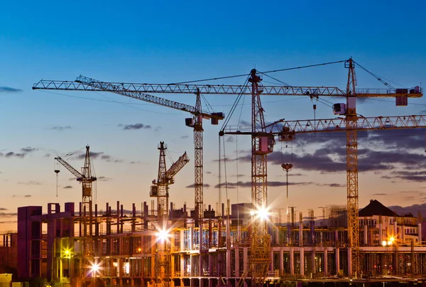 Silhuetas de guindastes de torre contra o céu da tarde. Casa em construção. Linha do horizonte industrial — Fotografia de Stock