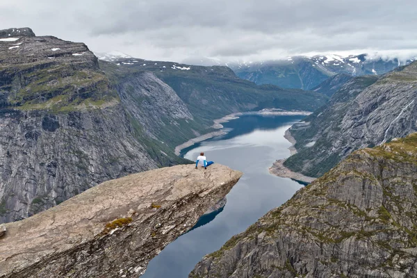 Mann sitzt auf Trolltunga-Felsen (Trollzungenfelsen) und blickt auf norwegische Berglandschaft — Stockfoto