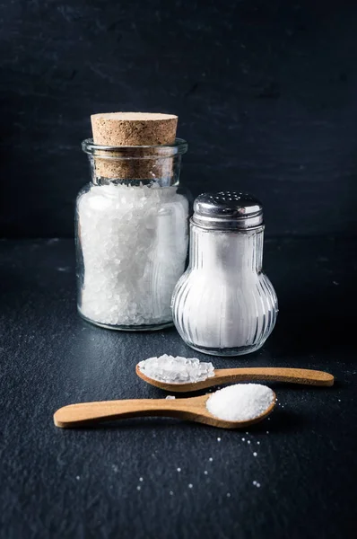 Tuz ile kaşık ve kavanoz koyu arka plan üzerinde farklı türleri. Deniz tuzu