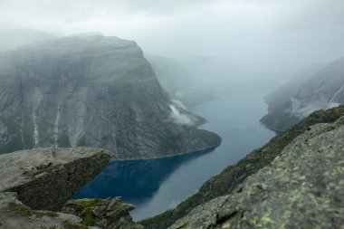 Norveç 'te, yağmurlu havada, dağların ve nehrin arka planında bir trolün dilinin ucunda bir adam.