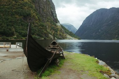 Nehrin arka planında eski Norveç Viking teknesi, dağlar ve mavi gökyüzü
