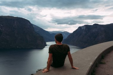 Bir adam siperin kenarında oturuyor. Norveç 'in arka planında ve gökyüzünde bulutlarla.